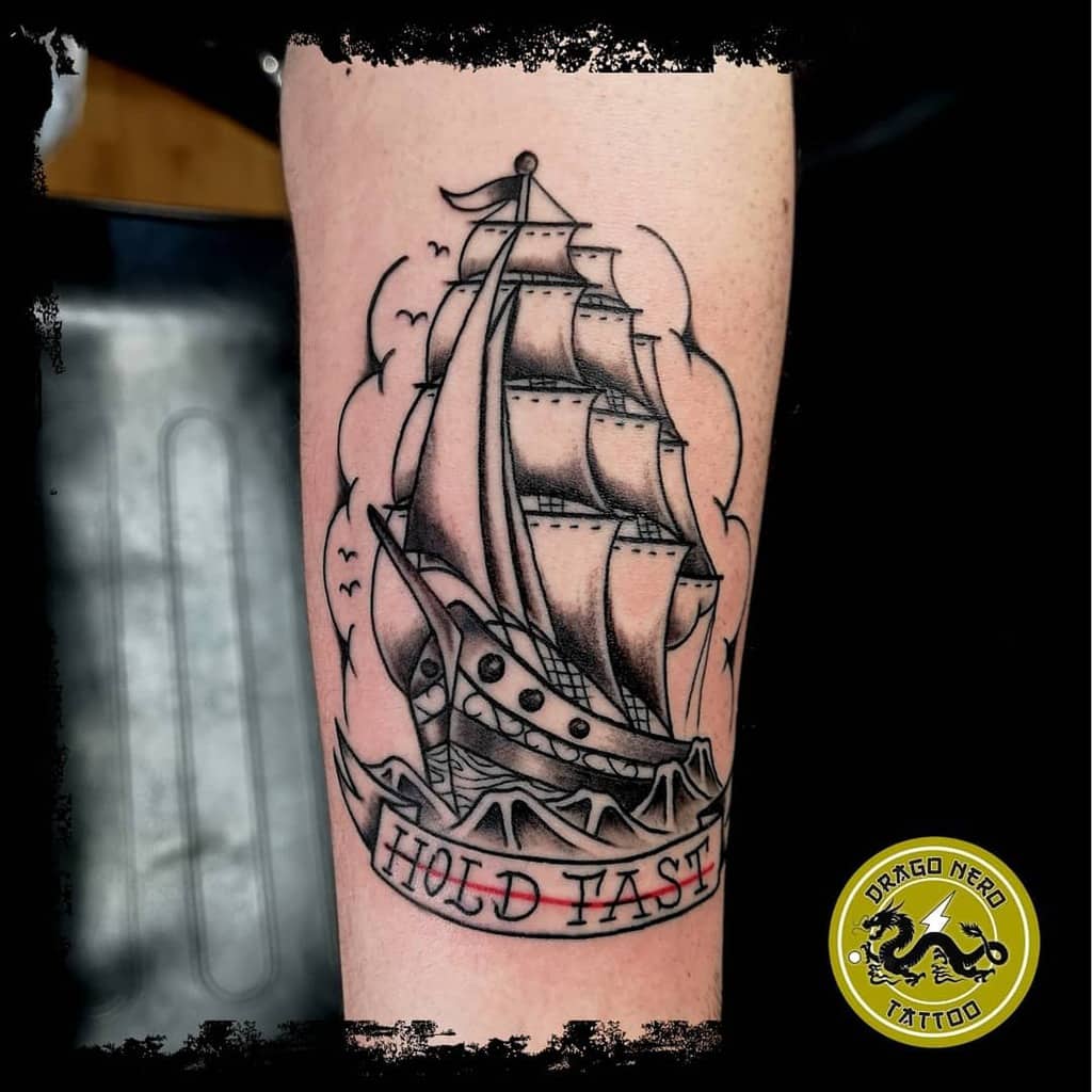 Tattoo of a sailing ship with "Hold Fast" text on an arm