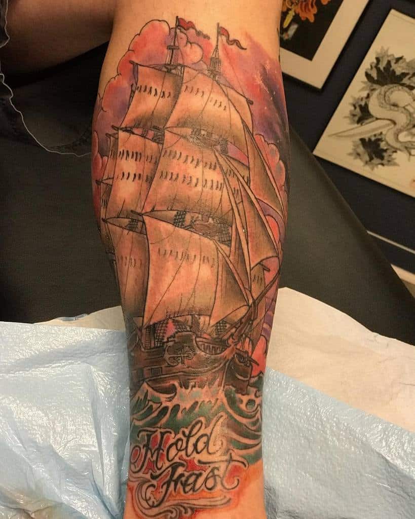 Tattoo of a sailing ship and waves with "Hold Fast" text on a forearm
