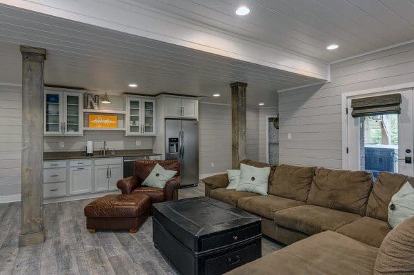Cozy basement with shiplap ceiling, recessed lighting, sectional sofa, and modern kitchenette.