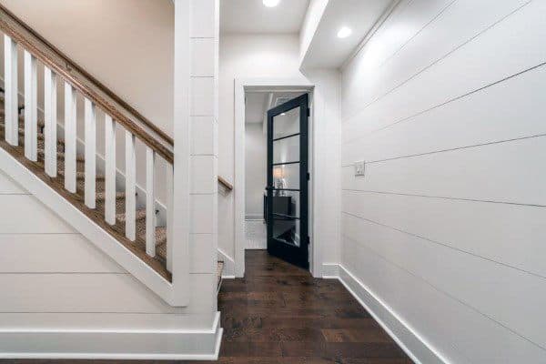 Hallway with white shiplap walls, a wooden staircase, and a black-framed glass door at the end
