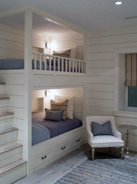 Cozy room with built-in bunk beds, stairs, an armchair, and soft lighting. Light walls and a rug on the floor