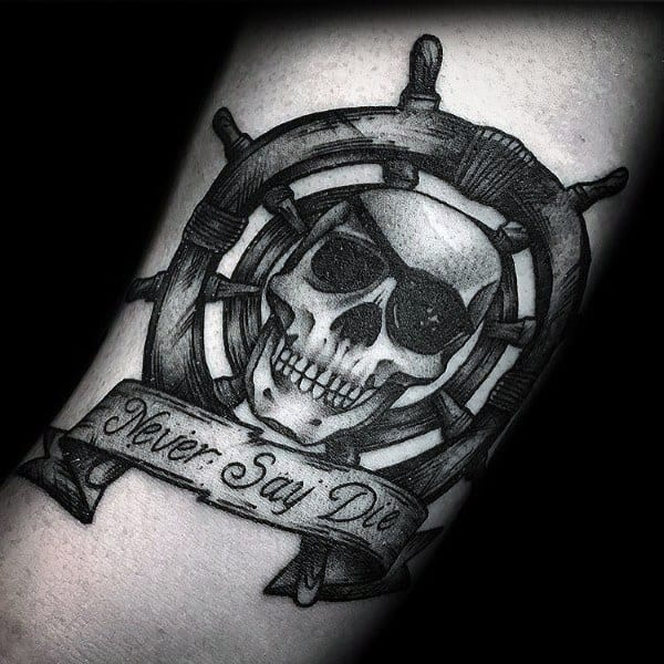 Black and gray tattoo of a skull with an eye patch inside a ship’s wheel, featuring a banner that reads "Never Say Die," inspired by The Goonies.