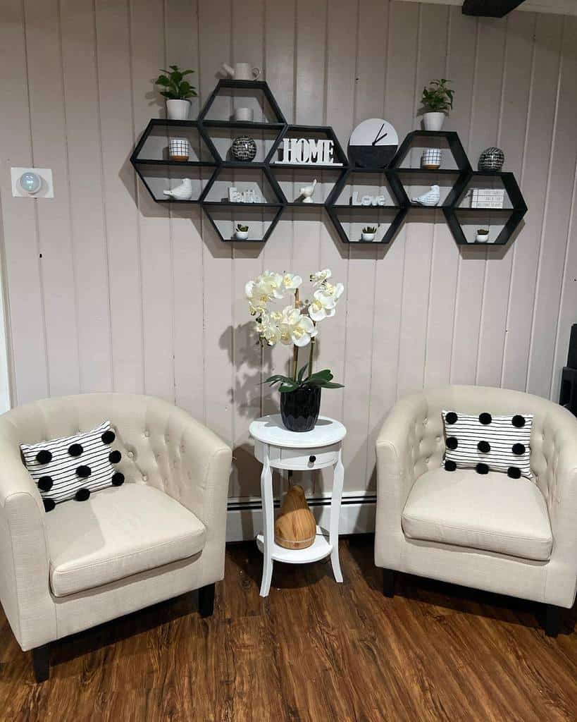 Cozy living room with tufted armchairs, wooden panel walls, and hexagonal wall shelves.