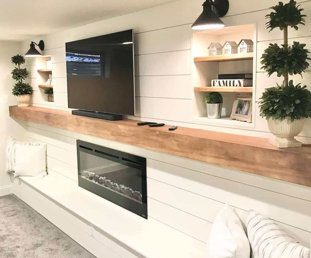 Modern basement living room with wall-mounted TV, electric fireplace, and built-in shelves.