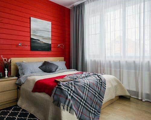 Cozy bedroom with a bold red accent wall, double bed, and large window with sheer curtains