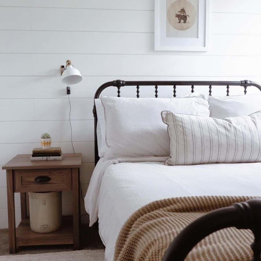 A cozy bedroom with a white bed, striped pillows, a wooden nightstand, and a framed bear print