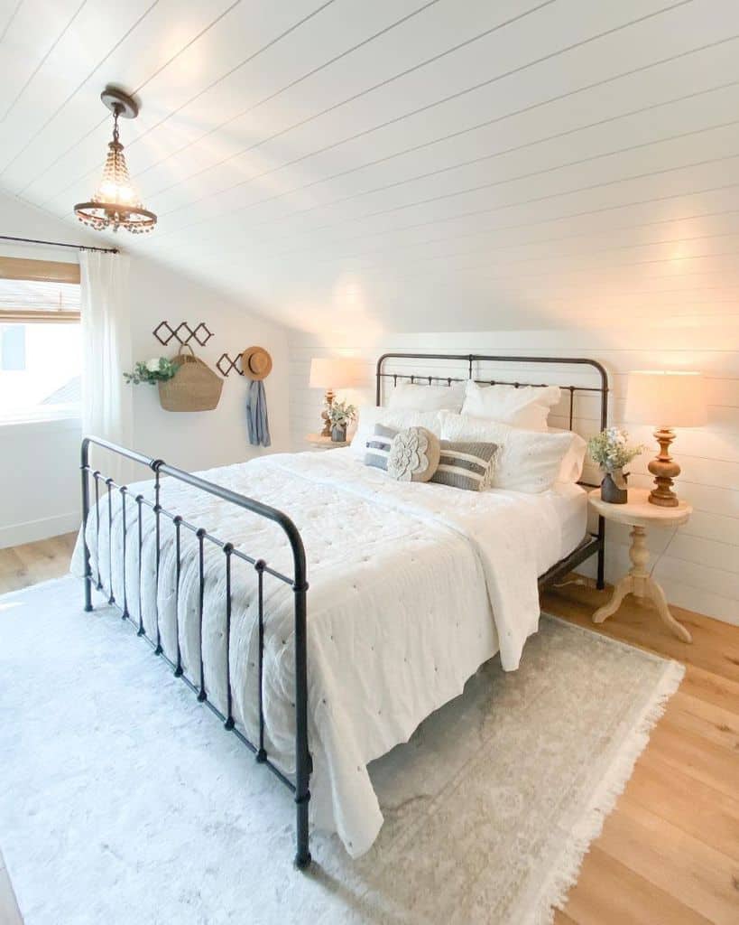 Cozy bedroom with a metal bed, warm lighting, rustic decor, and white bedding on a wooden floor