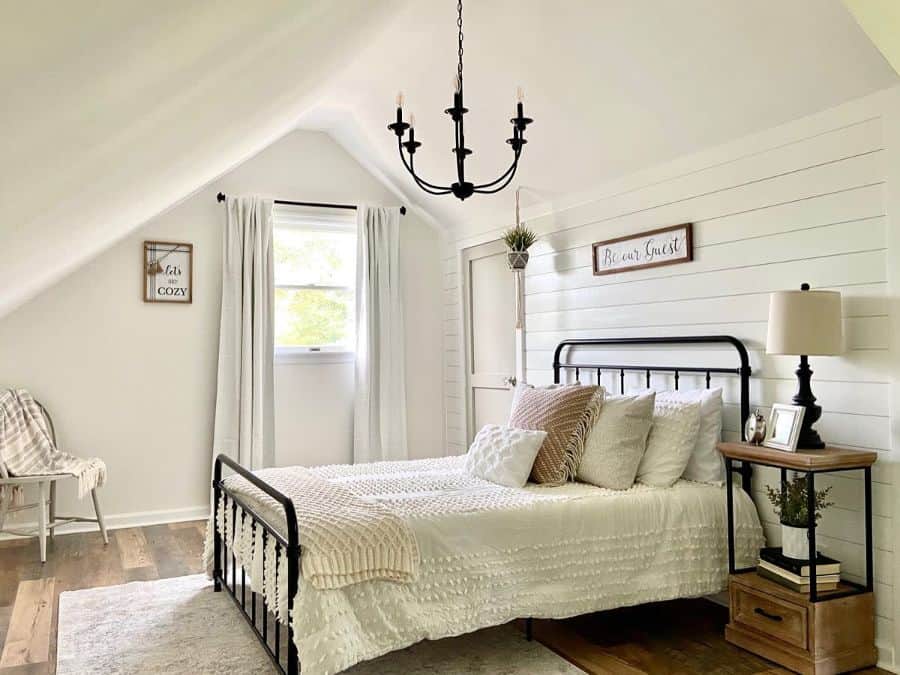 Cozy attic bedroom with a white metal bed, light decor, and chandelier under a sloped ceiling