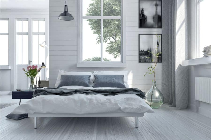Minimalist bedroom featuring a crisp white bed, gray pillows, large window, and framed black-and-white pictures on the wall