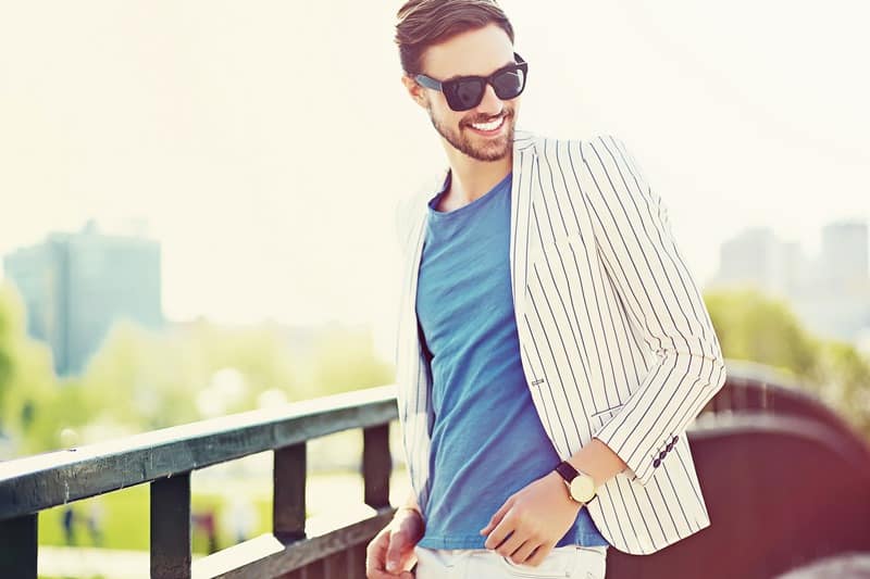 A man with a beard and sunglasses, wearing a blue shirt and a white striped blazer