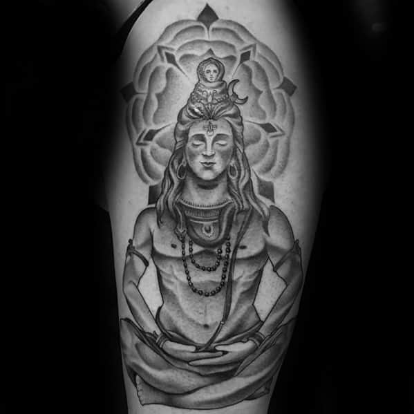 Tattoo of Lord Shiva in a meditative pose with closed eyes, seated in front of a large mandala lotus design, symbolizing peace and spiritual energy.