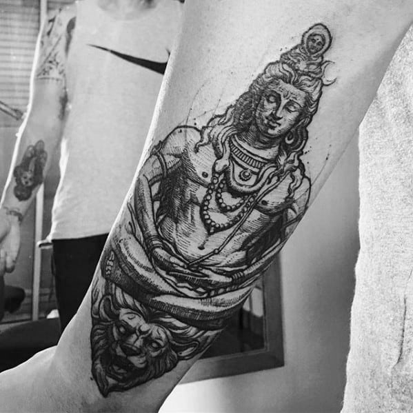 Forearm tattoo of Lord Shiva in a meditative pose, detailed with fine lines, seated on a roaring lion's head with symbolic ornaments.