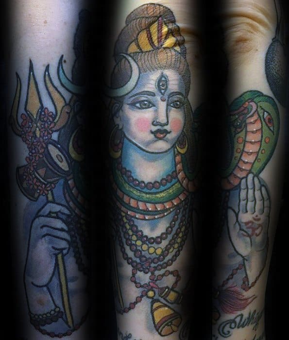 Colorful sleeve tattoo of Lord Shiva holding a trident, adorned with beads, crescent moon, cobra, and raised blessing hand in a divine pose.
