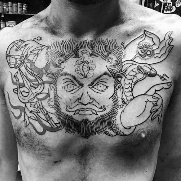 Bold chest tattoo of a fierce Shiva face with intense eyes and third eye, flanked by trishul, snake, damru, and symbolic hand gestures.