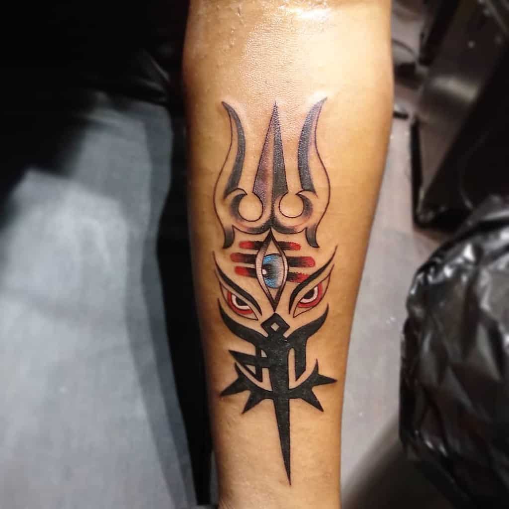 Tattoo of a trident with a third eye, red accents, and bold black tribal design, inked on the forearm.