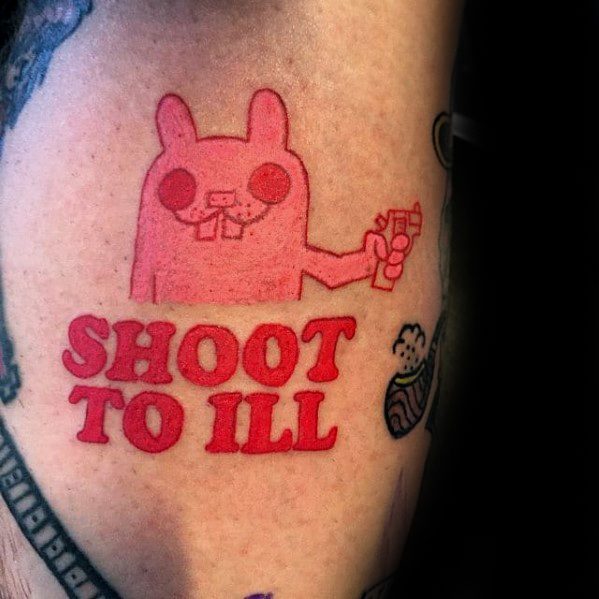 Bright red tattoo of a cartoon bunny holding a toy gun with bold text “SHOOT TO ILL” underneath, styled in a playful and quirky design.