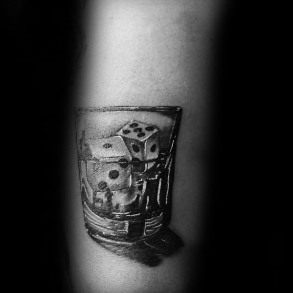 Realistic black and grey shot glass tattoo featuring dice inside, symbolizing luck and chance with detailed shading and depth.