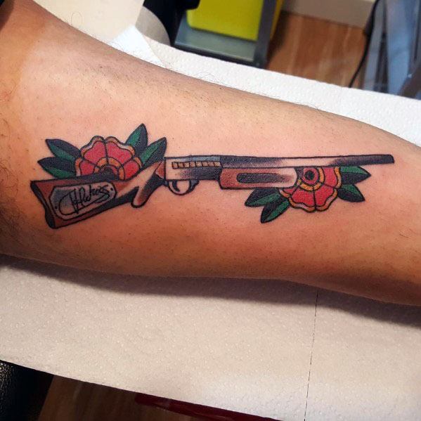 Traditional-style shotgun tattoo with red roses and green leaves, featuring bold outlines and vibrant colors for a striking and artistic design.