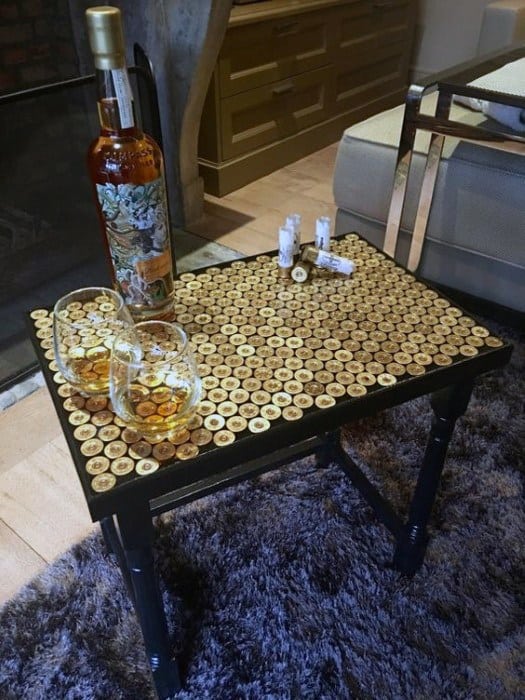 A coffee table with a top made of bottle caps, holding a bottle and glasses of whiskey