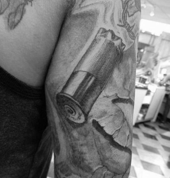 Realistic black and grey shotgun shell tattoo on the arm, featuring fine shading and a cracked background for a bold and dynamic effect.