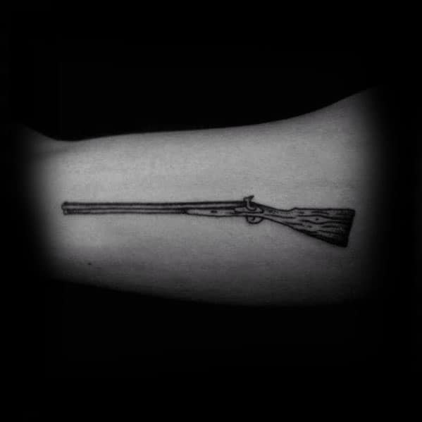 Minimalist rifle tattoo on the arm, featuring fine linework and subtle wood grain detailing for a sleek and understated design.