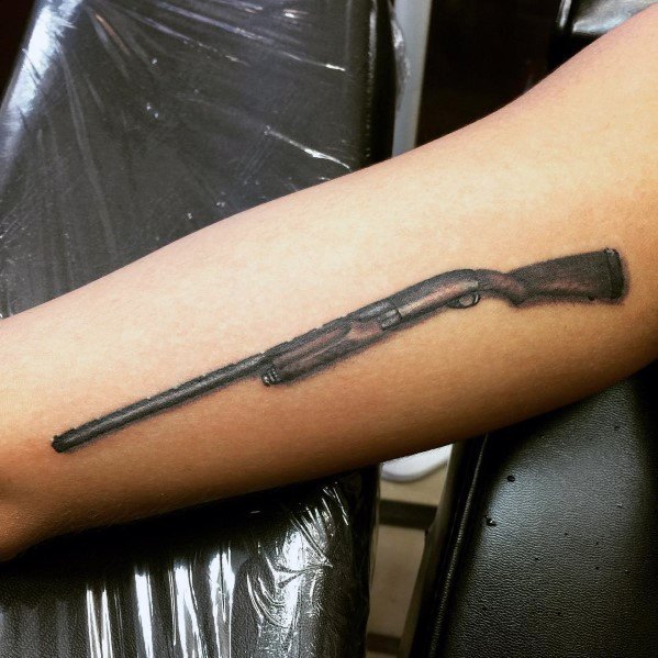 Realistic shotgun tattoo on the forearm, featuring fine details, black shading, and wood grain texture for a sleek and detailed firearm design.