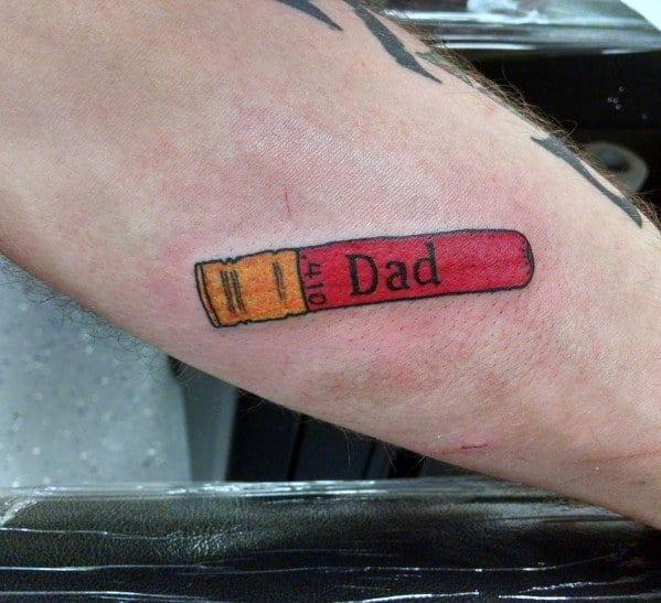 Minimalist shotgun shell tattoo with "Dad" written on the casing, featuring bold red and gold tones for a simple yet meaningful tribute design.