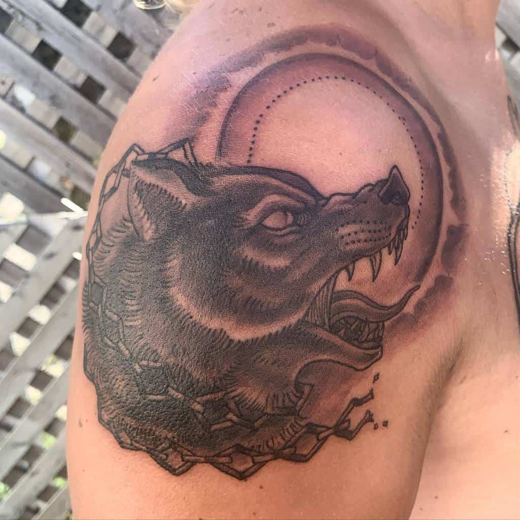 This striking shoulder tattoo features a fierce Norse wolf, surrounded by a symbolic circular design with shading that evokes the moon, representing power and primal energy