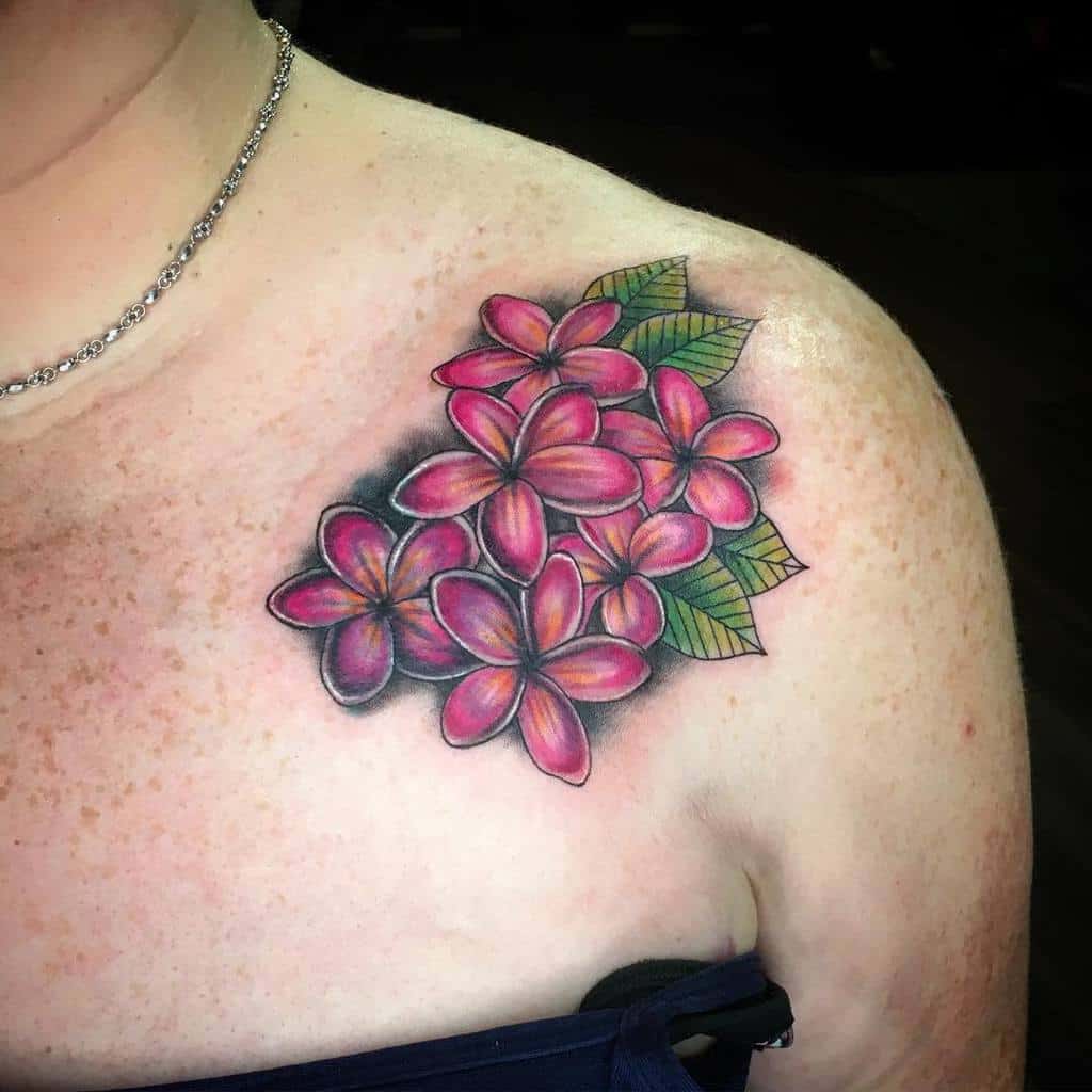 A stunning shoulder tattoo featuring a cluster of vivid pink Plumeria flowers accented with green leaves, creating a vibrant and tropical design