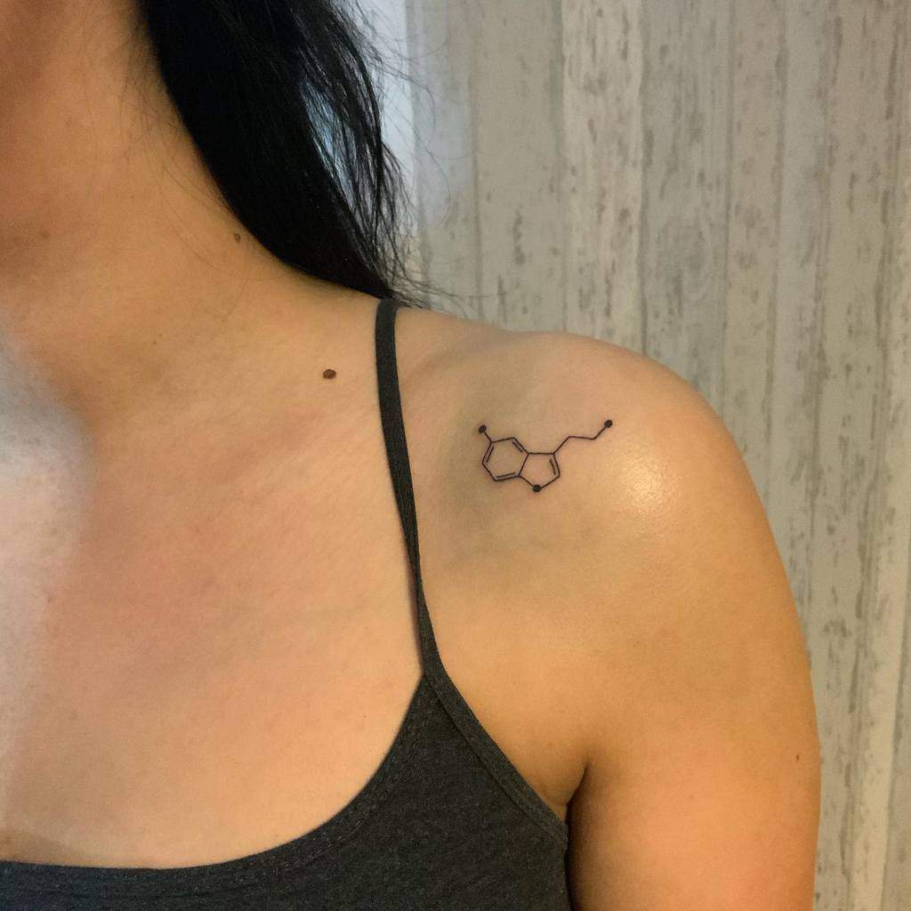 A woman proudly displays a tattoo of the serotonin chemical structure on her shoulder, symbolizing happiness and balance
