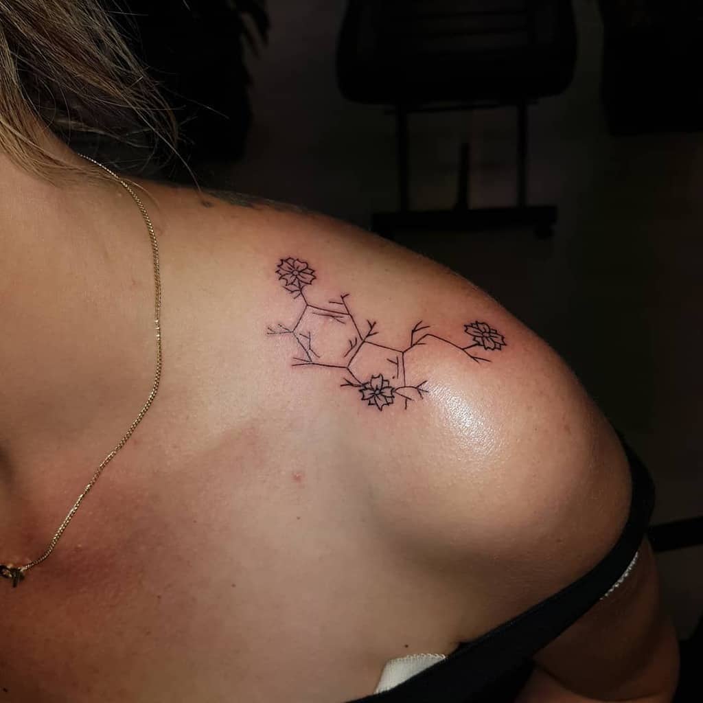 Delicate floral tattoo on a person's shoulder with small, intricate flowers and branches, creating a serotonin-inspired design that embodies tranquility and joy