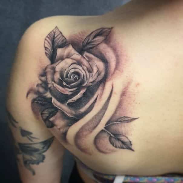 Realistic rose tattoo on a shoulder, featuring detailed shading and leaves