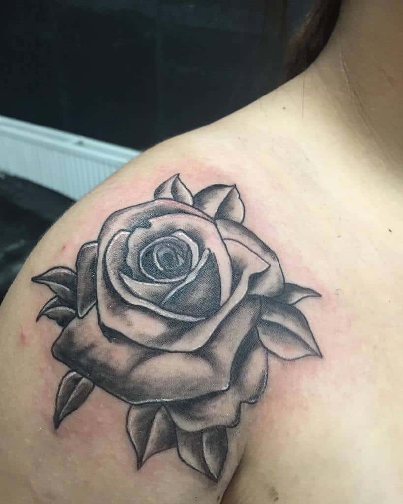 A black rose tattoo on a shoulder in grayscale