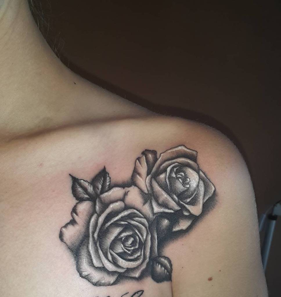 A stunning black and white tattoo elegantly features a rose, beautifully detailed, blooming across a person's shoulder