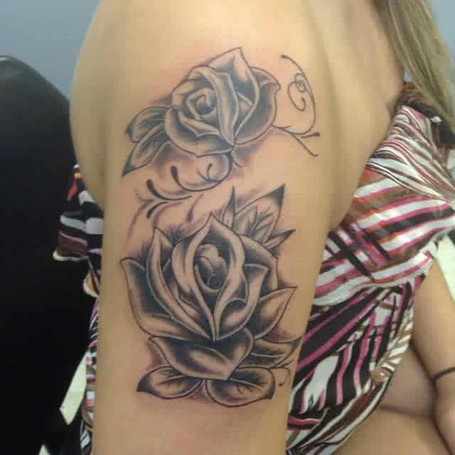 Two grayscale roses elegantly bloom on a person's upper arm, their delicate petals intricately captured in this stunning tattoo design