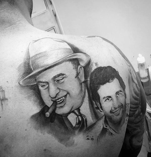 Al Capone tattoo on the back featuring a detailed black-and-white portrait of the gangster with a cigar, alongside another figure, likely a reference to a person from his era or a popular figure related to him.