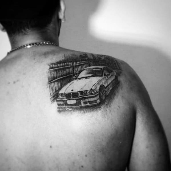 Realistic BMW E36 tattoo on upper back, featuring fine details and a background fence for a dynamic and personal automotive design.