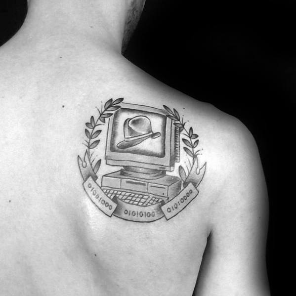 Shaded black and grey tattoo of a vintage computer with a hat on the screen, framed by laurel leaves and binary code banners.