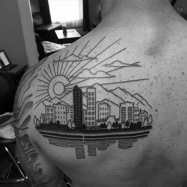 Minimalist Denver skyline tattoo on upper back with sun rays, mountains, city reflection, and fine line detailing of buildings and trees.