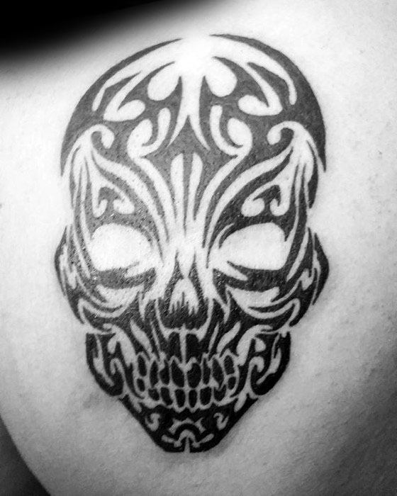 Tribal skull tattoo with bold black symmetrical patterns, hollow eyes, and detailed linework for a clean, stylized look on the shoulder.