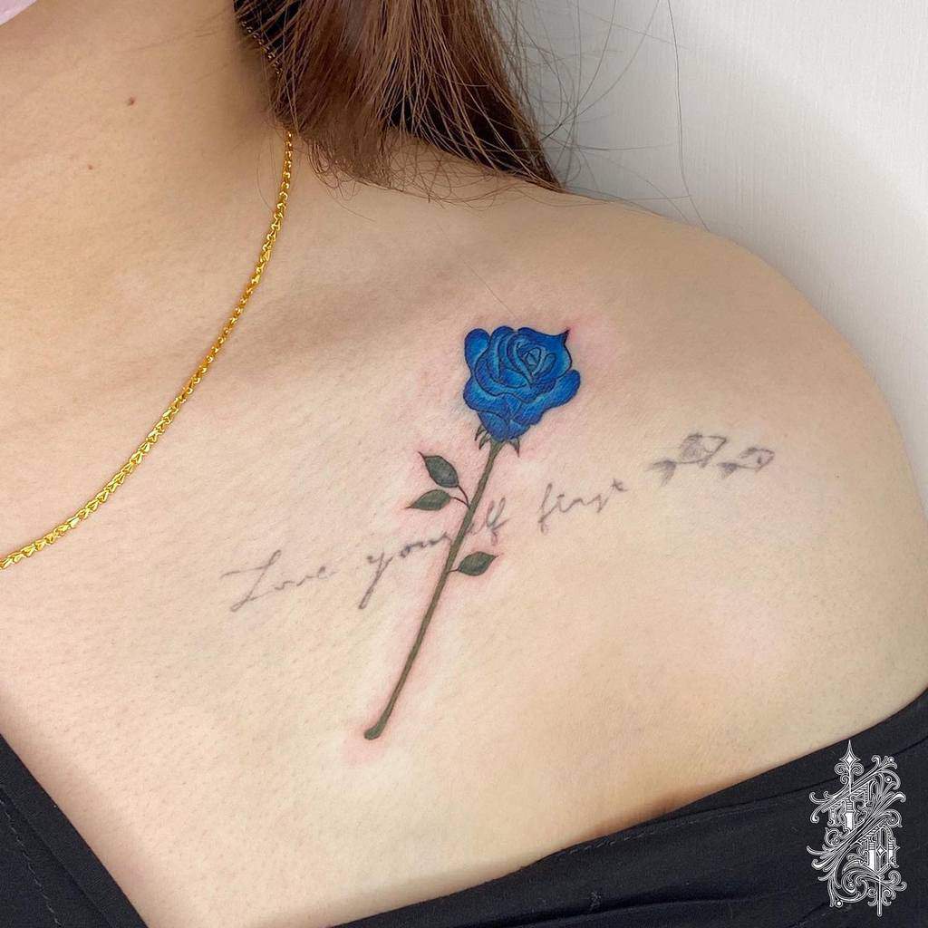 A beautiful tattoo of a blue rose graces the shoulder, elegantly intertwined with the inspiring words "Love yourself first"