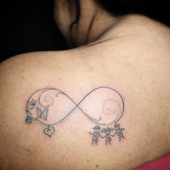 A meaningful infinity tattoo featuring a bird, heart, and three figures holding hands, representing eternal love, family, and connection.