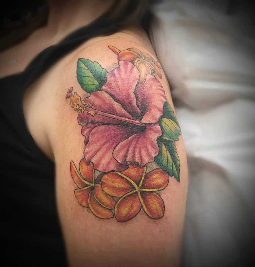 Colorful shoulder tattoo featuring a large pink hibiscus flower with detailed green leaves, accompanied by vibrant orange and yellow plumeria flowers