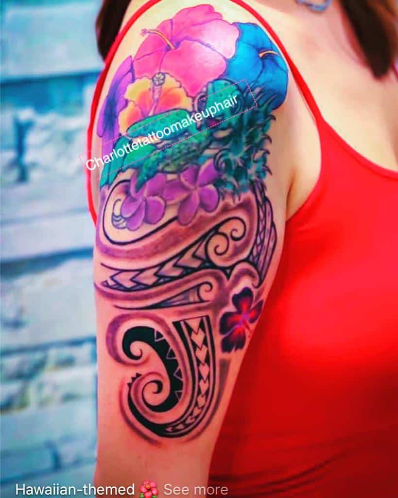 Colorful shoulder tattoo featuring vibrant pink and blue hibiscus flowers, with black tribal designs and swirls