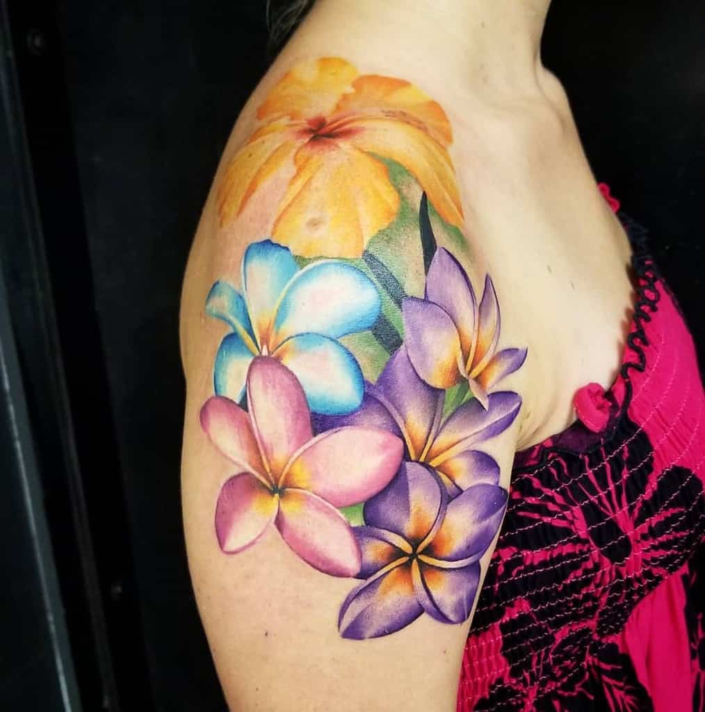 Vibrant shoulder tattoo featuring a cluster of colorful plumeria flowers in shades of pink, blue, purple, and yellow, creating a tropical floral design