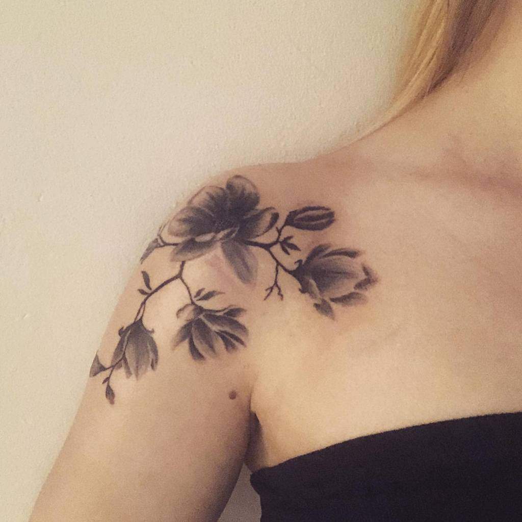 A magnolia tattoo graces a woman's shoulder, featuring beautifully shaded flowers and leaves