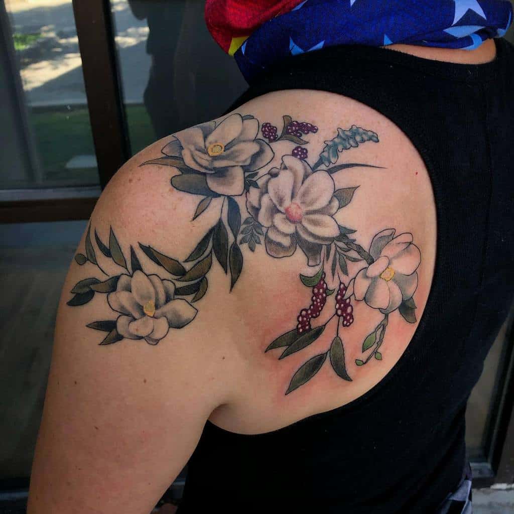 The tattoo features a detailed and elegant design of magnolia flowers on the shoulder, with soft shading, rich colors, and delicate leaves, creating a harmonious and natural look that flows gracefully along the arm