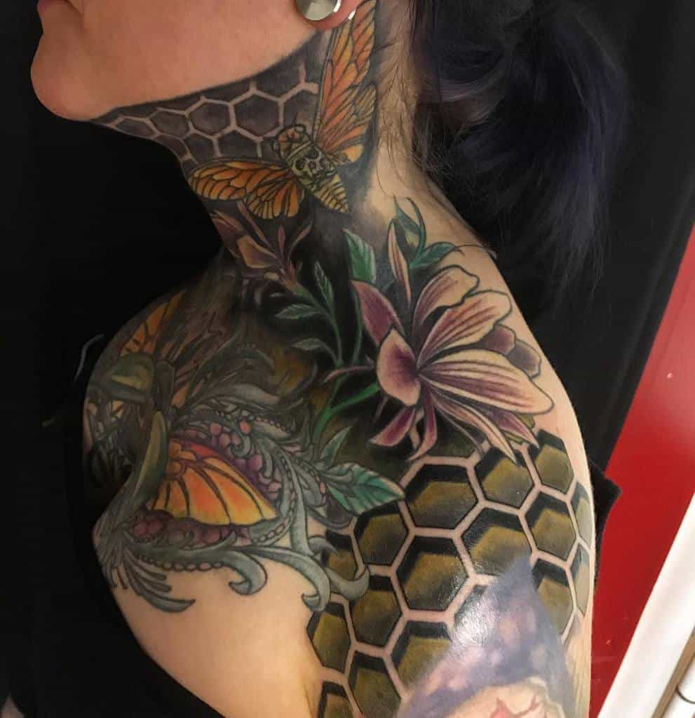 Woman with colorful floral, magnolia, butterfly, and honeycomb tattoos on neck and shoulder