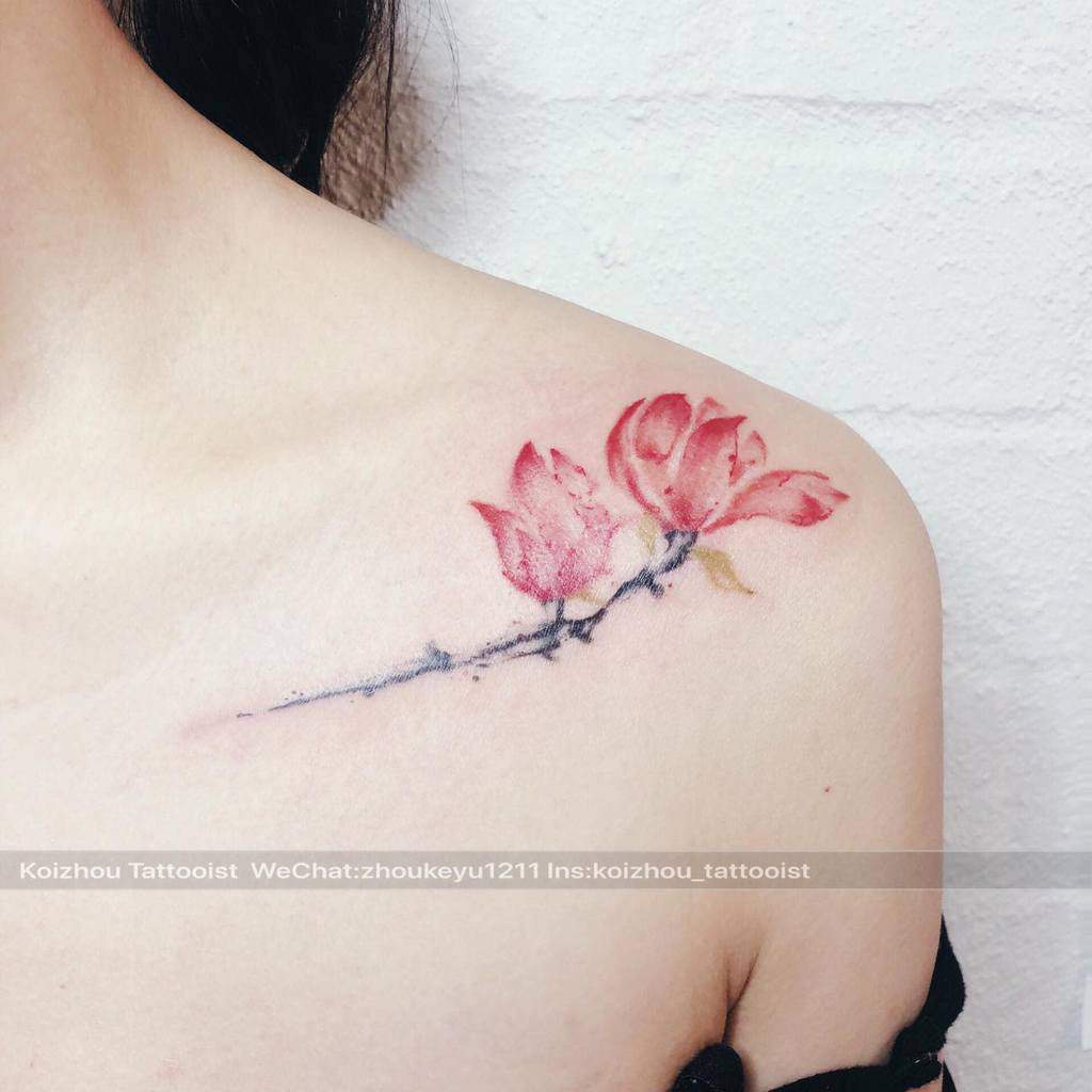 A pink cherry blossom and magnolia tattoo adorns a person's shoulder