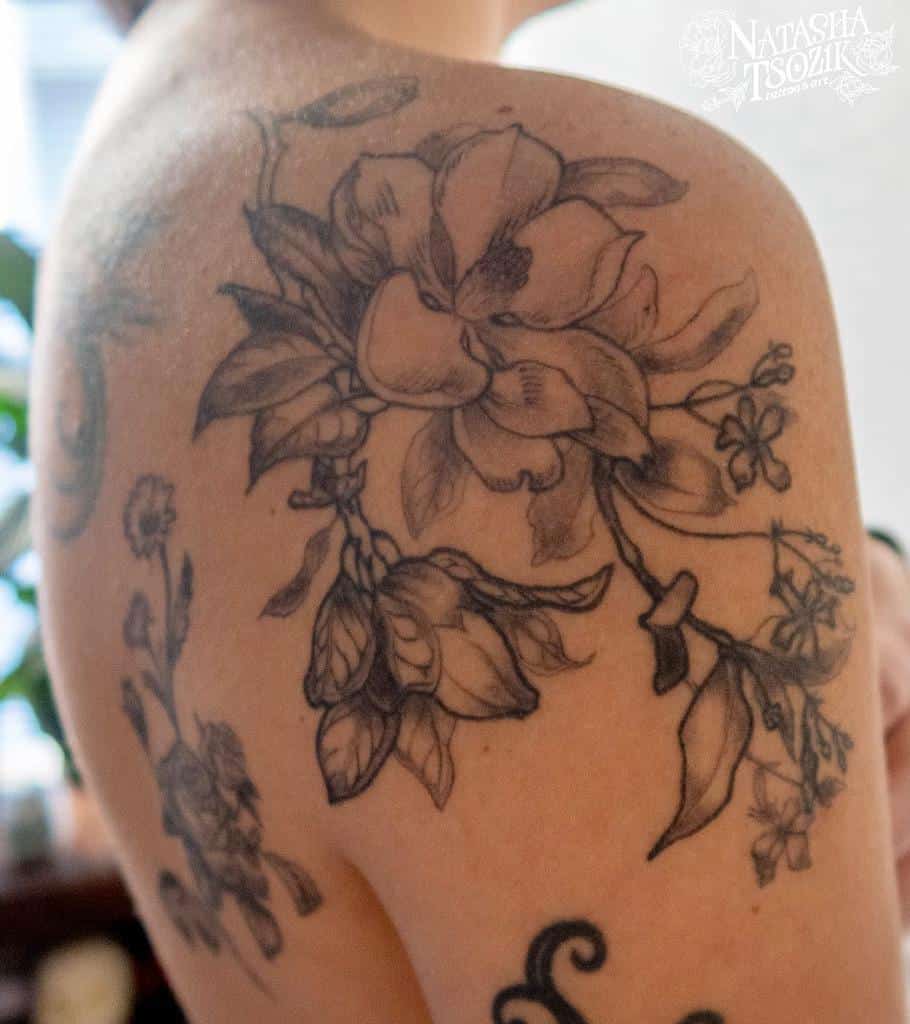 A shoulder tattoo showcasing detailed magnolia flowers and leaves in black ink